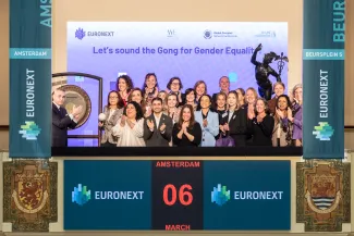 A group of International Women’s Day participants posing together beside a large ceremonial gong, smiling and celebrating the event.