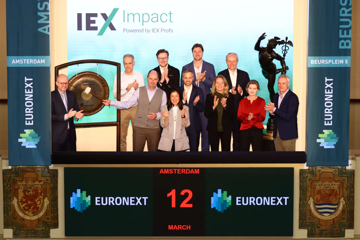 A group celebrates the launch of IEX Impact as the ceremonial gong is struck, with guests and organisers gathered around.