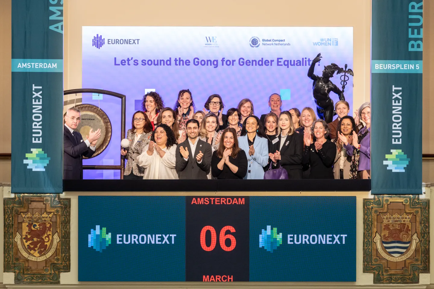 A group of International Women’s Day participants posing together beside a large ceremonial gong, smiling and celebrating the event.