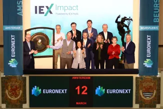 A group celebrates the launch of IEX Impact as the ceremonial gong is struck, with guests and organisers gathered around.